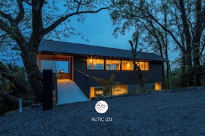 A modern house with a covered porch, large windows, and a gravel driveway. - Nutic Izu (Ito)