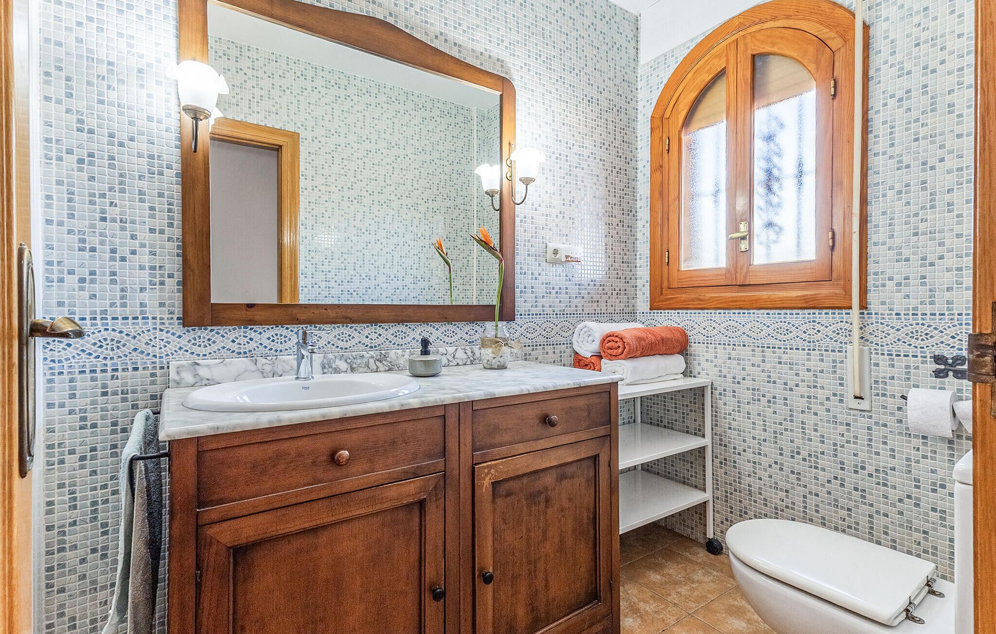 Un baño con dos lavamanos, un espejo, un armario de madera, un inodoro y una ventana con vidrio esmerilado.