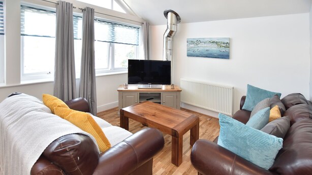 Ett vardagsrum med två soffor klädda i läder, ett soffbord i trä, en platt-TV på ett träställ och en tavla som föreställer ett kustlandskap på väggen.