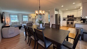 A spacious living area with a dining table, chairs, and a kitchen in the background.