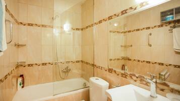 Een badkamer met bad, toilet en wastafel, met behang van beige tegels en een spiegel.