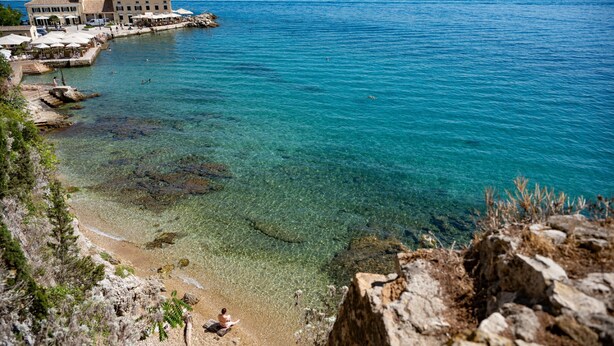 Un hotel frente al mar con aguas azules cristalinas, una playa y un barco en la lejanía.