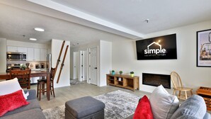 A modern living room with a grey sofa, red cushions, a grey ottoman, and a fireplace. There is a TV mounted on the wall displaying 'simple vacation rentals'.
