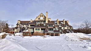 A large, multi-story building with a prominent clock tower, multiple balconies, and a snow-covered landscape.