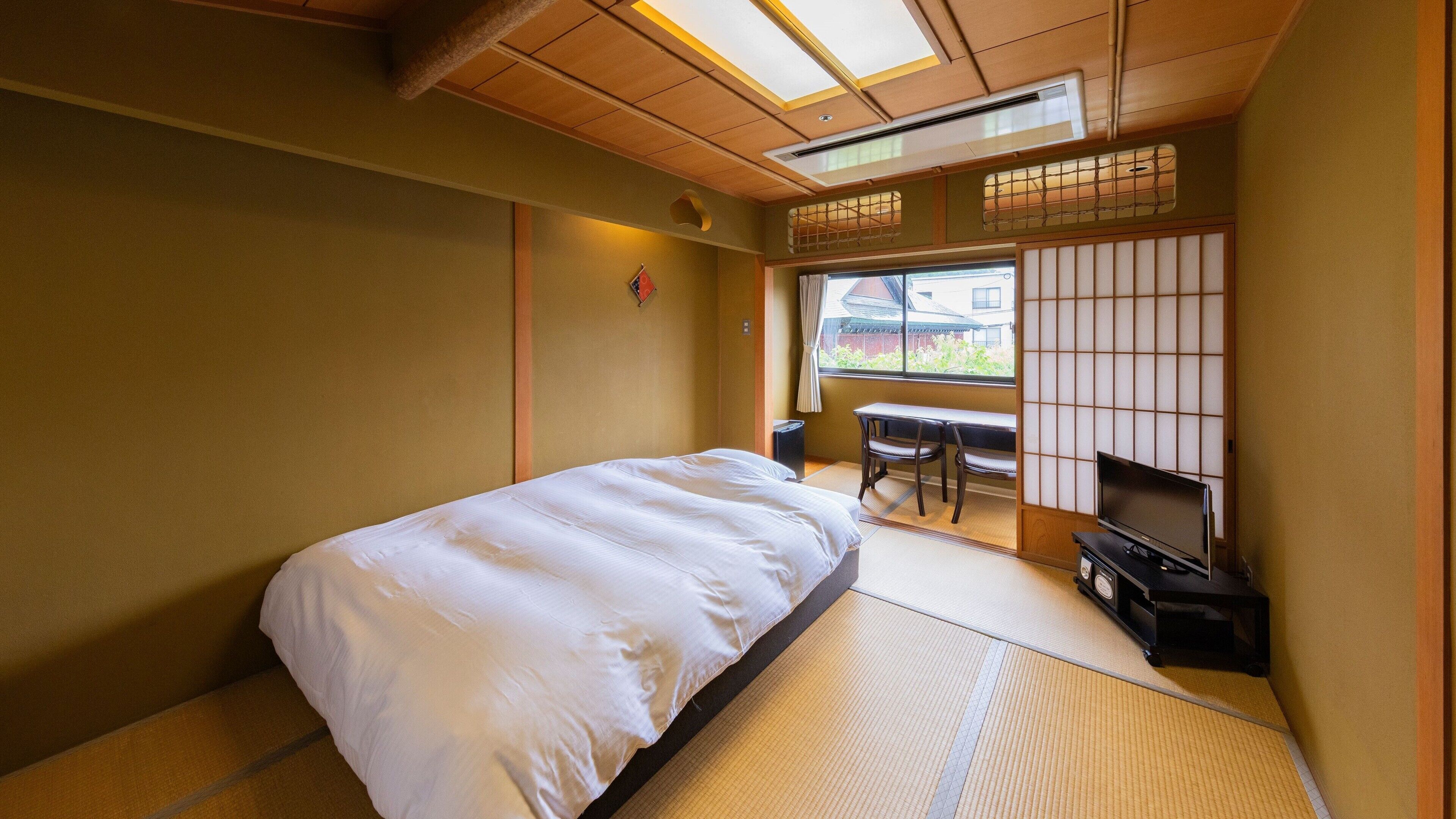Une pièce de style japonais traditionnel, avec un sol recouvert de tatamis, un lit, un bureau et un téléviseur.