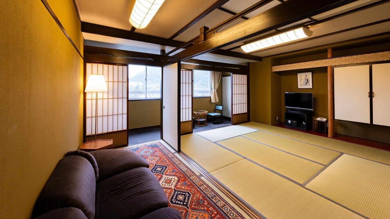 Une pièce de style japonais traditionnel, avec un sol recouvert de tatamis, un futon servant de lit, une télévision et des portes coulissantes donnant sur un balcon.