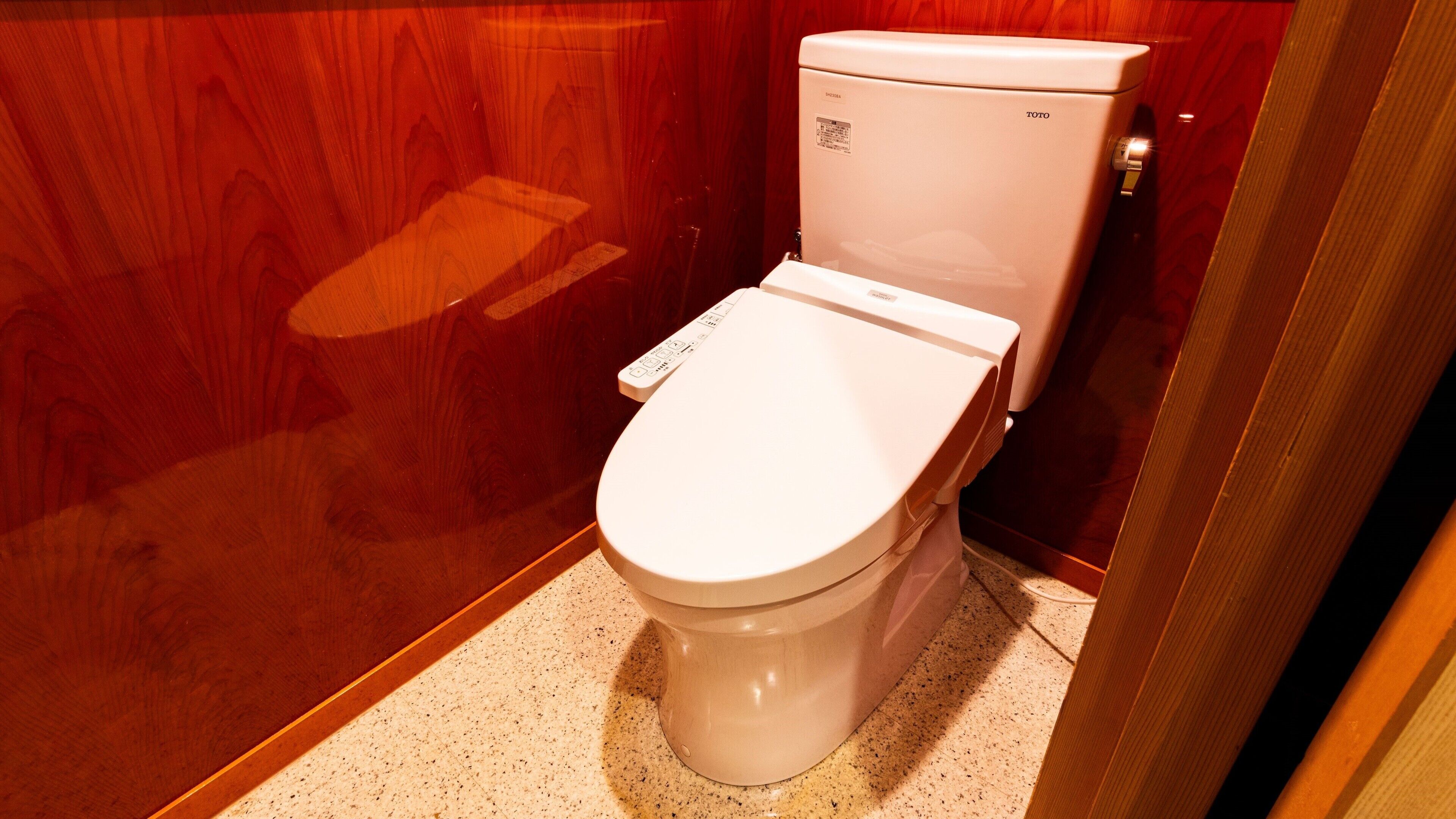 Des toilettes blanches dotées d’un panneau de commande, un mur en bois et un sol carrelé dans une salle de bain.