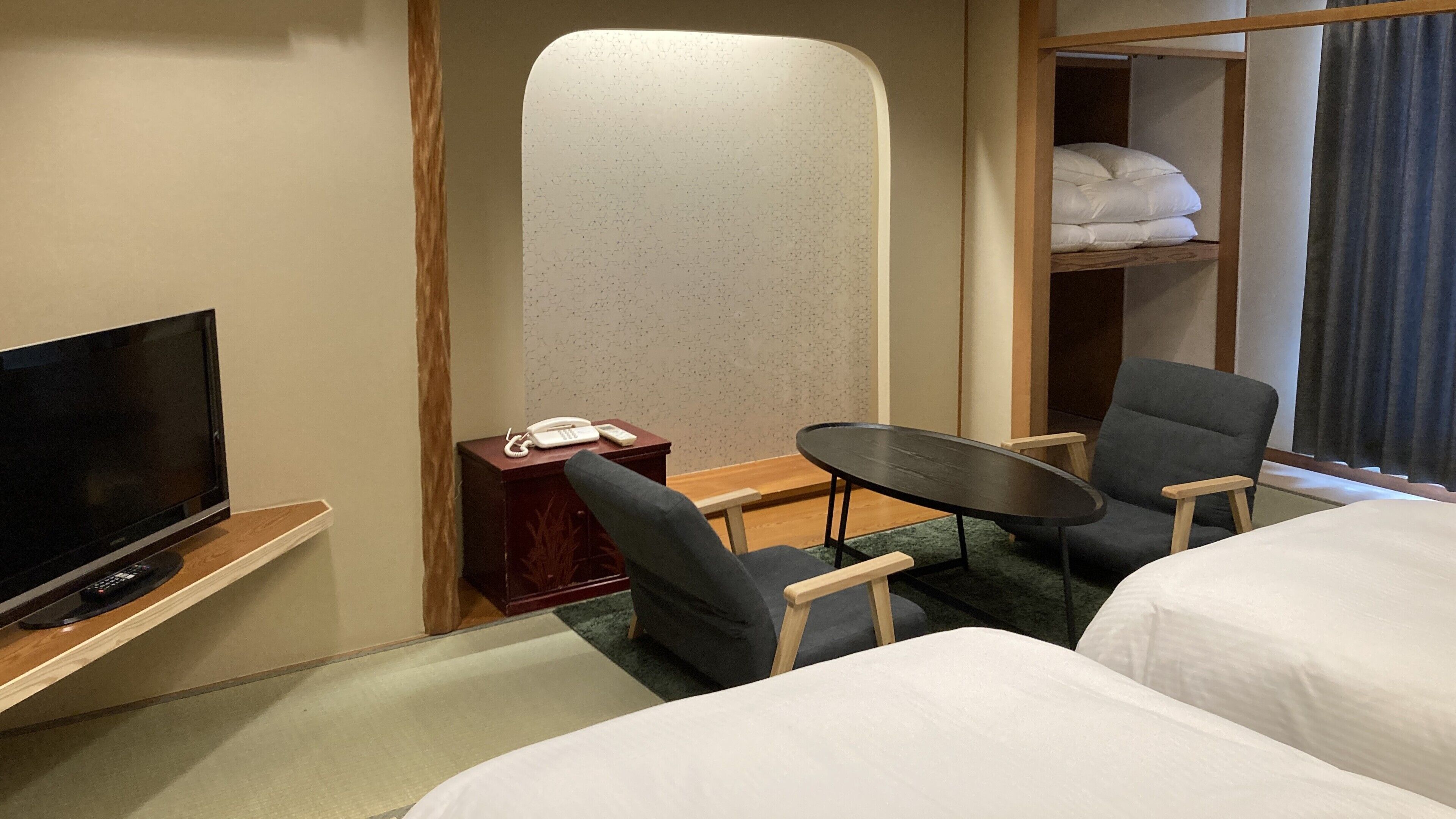 Une chambre d’hôtel équipée d’une télévision, d’un bureau avec un téléphone, de deux chaises, d’une petite table et d’un lit.
