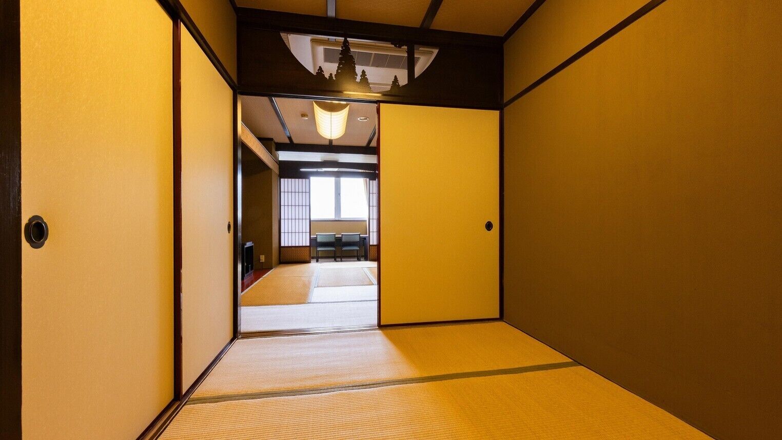 Une pièce de style japonais traditionnel, avec un sol recouvert de tatamis, des portes coulissantes et un luminaire au plafond.