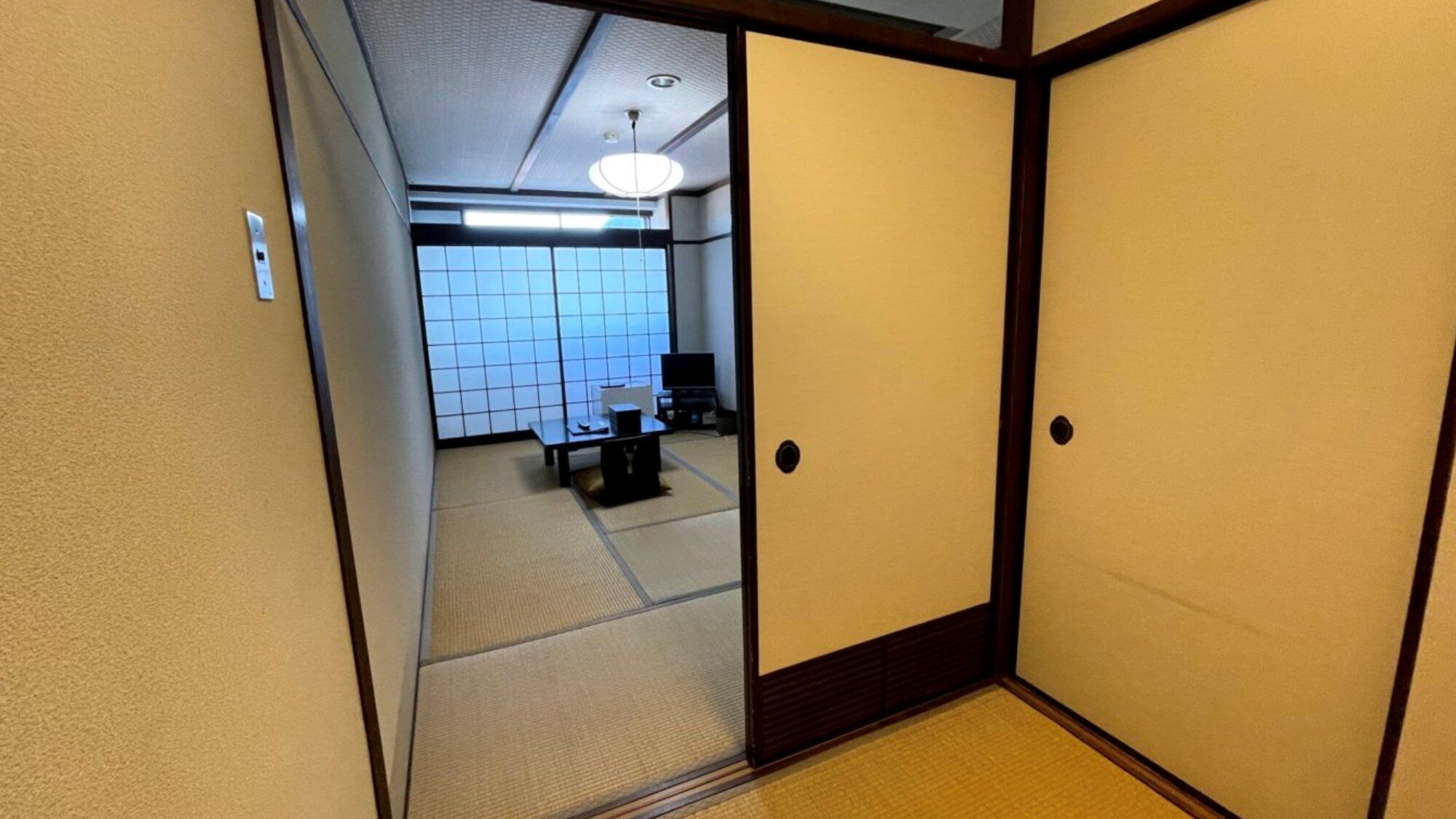 Une pièce de style japonais traditionnel, avec un sol recouvert de tatamis, un paravent en papier de riz (shoji) et un téléviseur.