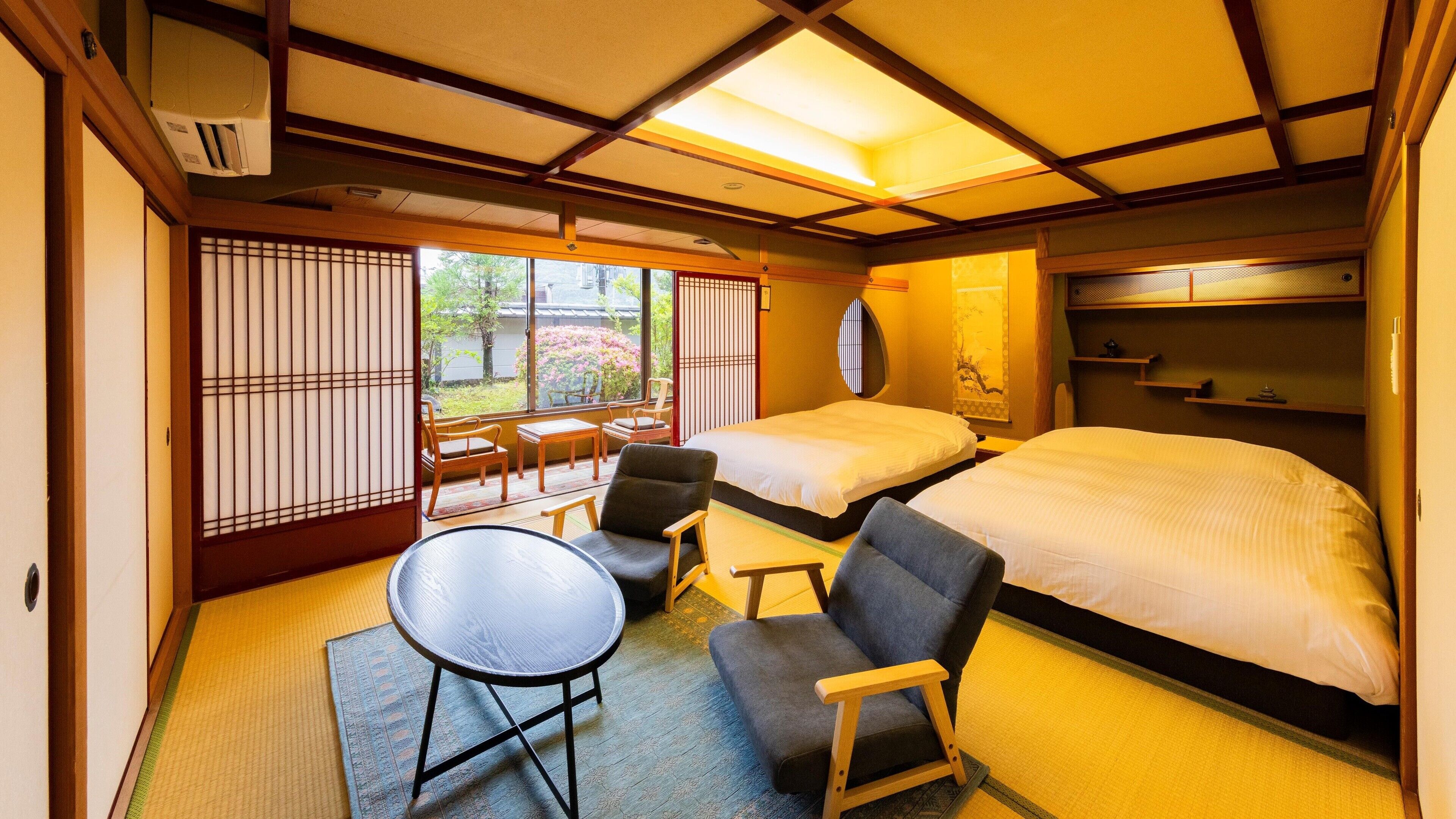Une pièce de style japonais traditionnel, avec un sol recouvert de tatamis, un futon servant de lit, une petite table ronde et une porte coulissante donnant sur un jardin.