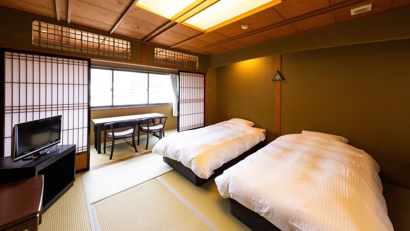 Une pièce de style japonais traditionnel, avec un sol recouvert de tatamis, une télévision, un bureau et deux lits.