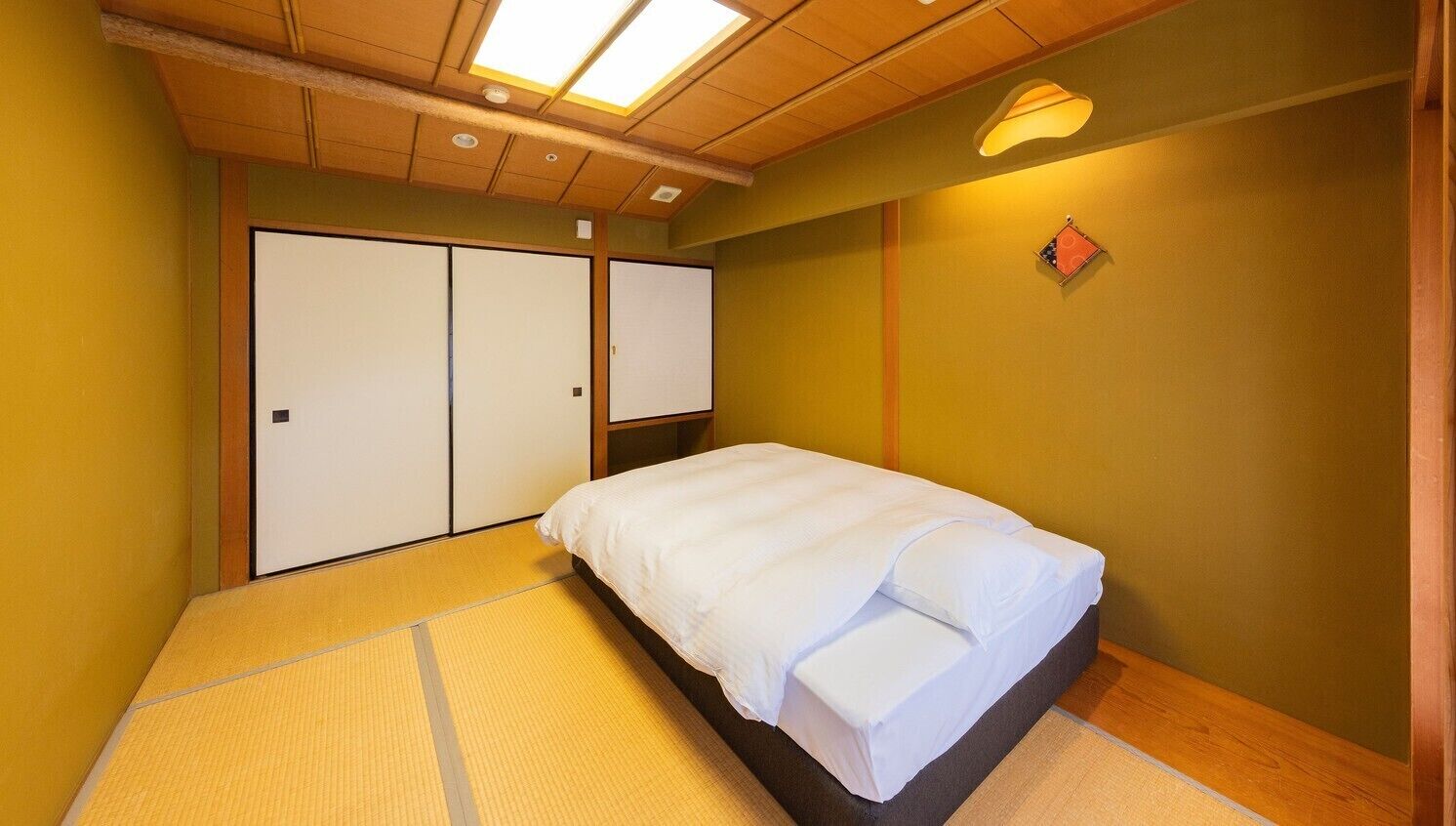 Une pièce comprenant un lit, un revêtement de sol en tatami, des portes coulissantes et un luminaire au plafond.