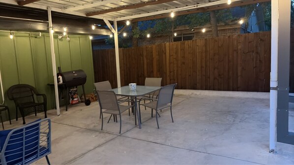 An outdoor patio area with a table and chairs, a grill, and a wooden fence.