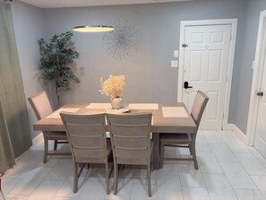 A dining area with a rectangular table, six chairs, a vase with flowers, a hanging light fixture, a wall decoration, and a door. - TEXANO INN Charming 3-bedroom house with WiFi and AC in welcoming Fort Worth (Fort Worth)