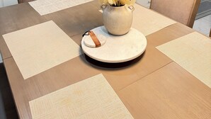 Un comedor con una mesa preparada para dos, un florero con flores amarillas y una cocina al fondo.