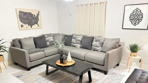 Una sala de estar moderna con un sofá seccional gris, una mesa de centro negra y una alfombra estampada.