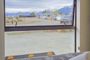 Una habitación con un amplio ventanal que da a un estacionamiento con vehículos y montañas al fondo.