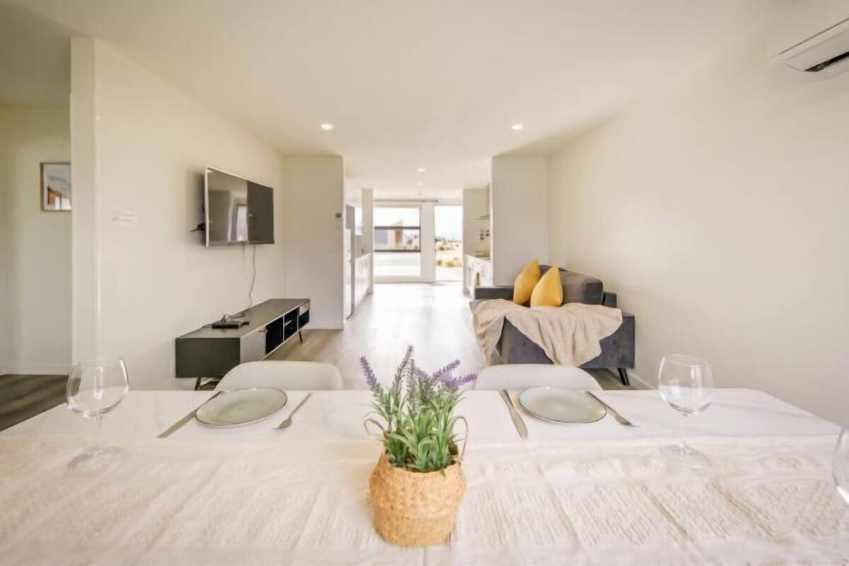 Un coin repas avec une table dressée pour deux personnes, un téléviseur fixé au mur et un canapé en arrière-plan.