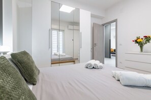 Una habitación de hotel moderna con una cama grande, un armario con espejo, una mesita de noche y un jarrón con flores.