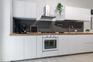 Una cocina moderna con armarios blancos, una campana extractora de acero inoxidable, un horno empotrado y una cafetera.