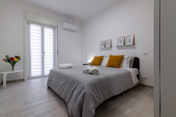Un dormitorio con cama, un banco, un florero con flores y una puerta con persianas.