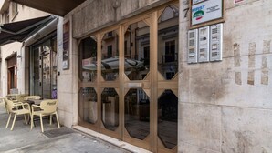 Ein Gebäude mit großer Glasfassade, Außenbereich mit Coca-Cola Stühlen und einem Schild, das eine Pianobar anzeigt.