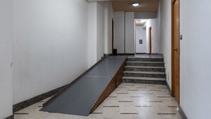 Ein Flur mit einer Rampe, die zu einer Treppe führt, einer Deckenleuchte und einer Tür rechts.