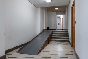 Un pasillo con una rampa que lleva a una escalera, una luz en el techo y una puerta a la derecha.