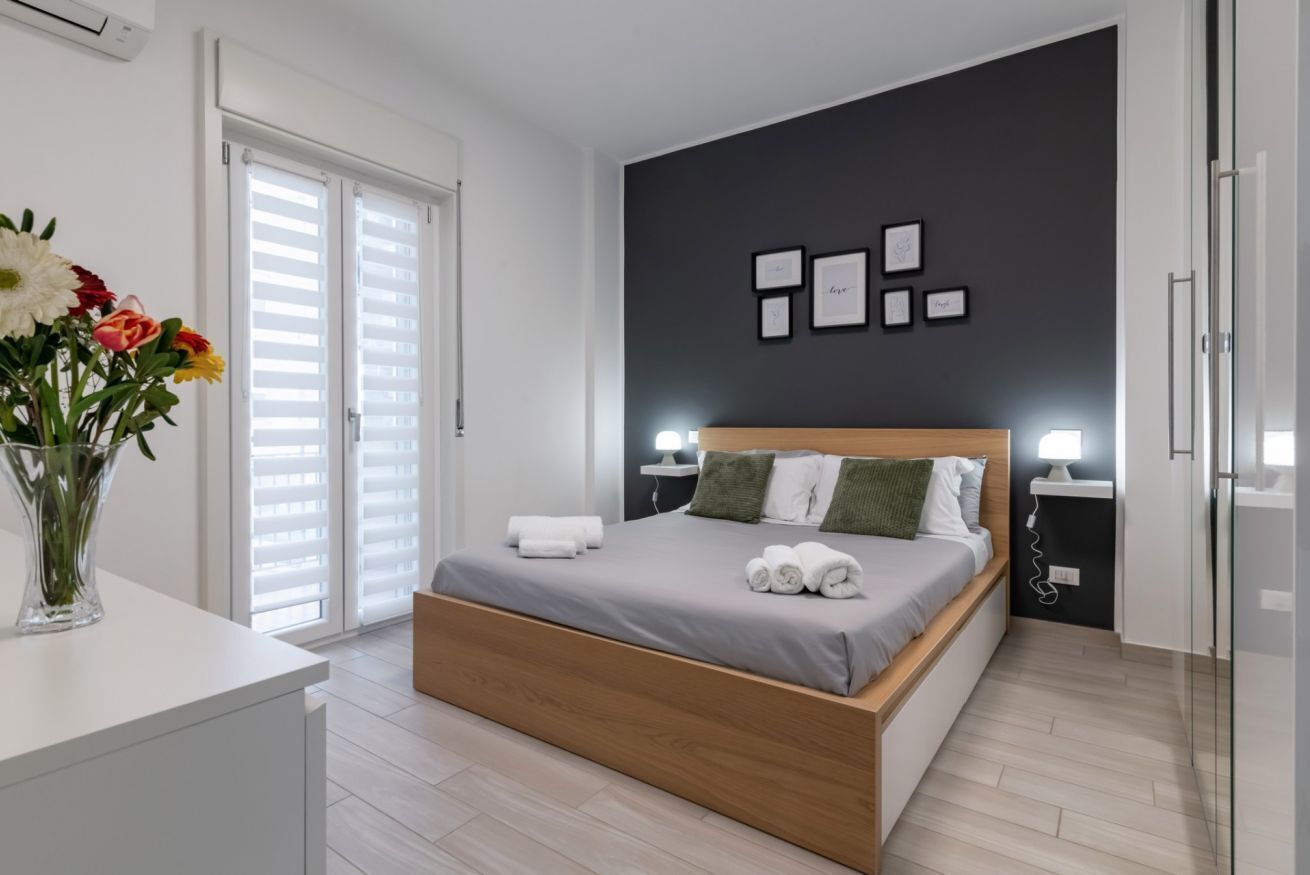 Une chambre à coucher moderne, avec un lit, des tables de chevet, un vase de fleurs et un mur orné de tableaux encadrés.