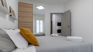Ein Schlafzimmer mit einem Bett, Kissen, einem Spiegel, einer Tür und einem Fenster.
