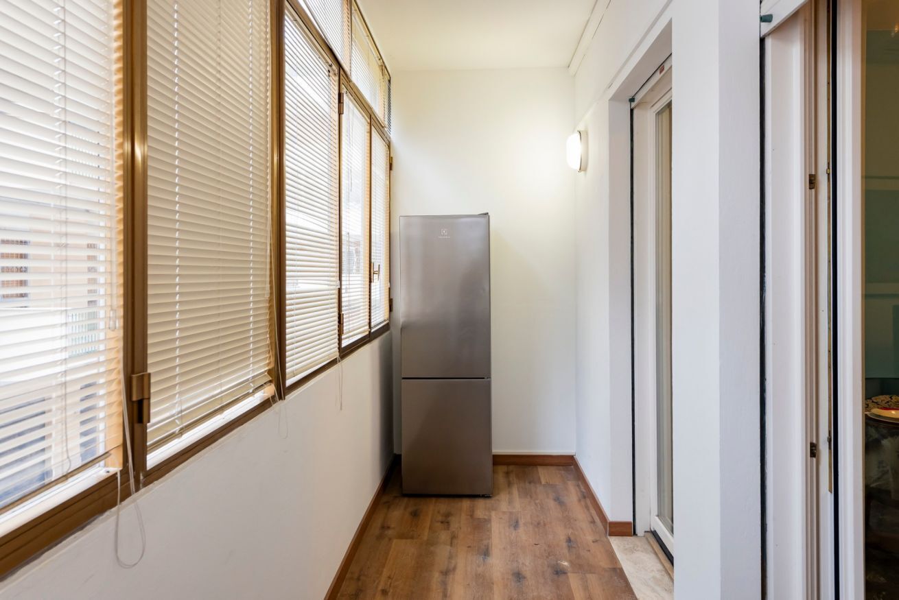 Un couloir étroit avec un plancher en bois, un réfrigérateur en acier inoxydable et une porte coulissante en verre.