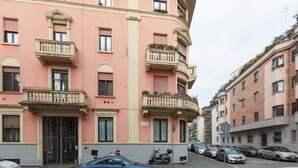 Un immeuble à plusieurs étages doté de balcons, avec des voitures garées et un passage piéton.