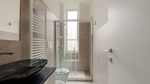 Une salle de bain moderne dotée d’une douche à parois de verre, de toilettes et d’un plan de toilette noir.