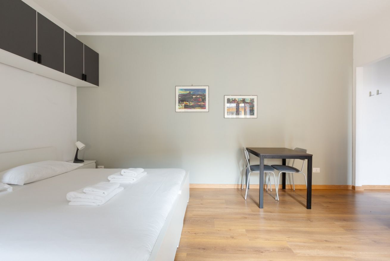 A hotel room with a bed, a desk, two framed pictures on the wall, and a wardrobe.