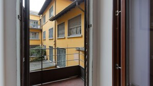 Une vue depuis un balcon sur un immeuble jaune, avec des fenêtres grillagées et une rambarde en métal.