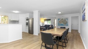 Eine moderne Küche mit weißen Schränken, einem Edelstahlkühlschrank und einem Essbereich mit Holztisch und schwarzen Stühlen.