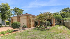 Ein Bungalow mit Garage, einer überdachten Veranda und einem kleinen Garten mit verschiedenen Pflanzen und Rasen.