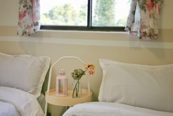 A bedroom with two beds, a bedside table with a pink lantern and flowers, and floral curtains.
