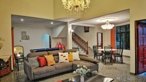 A spacious living area with a sofa, coffee table, and a chandelier. There is a staircase leading to another level, and a dining area with chairs and a table. - Yussy Homestay at Afamosa Bungalow (Pegoh)