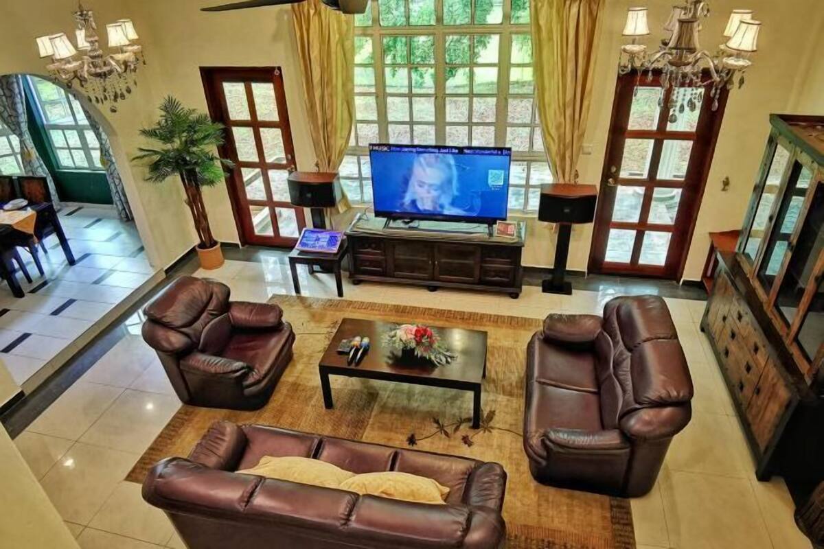 A living room with leather sofas, a coffee table, a TV, and a large window with curtains.