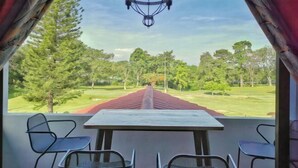 A dining area with a table and chairs, a chandelier, and a view of a golf course. - Yussy Homestay at Afamosa Bungalow (Pegoh)