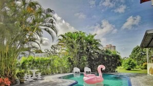 A swimming pool with a pink flamingo float, surrounded by lush greenery and white chairs. - Yussy Homestay at Afamosa Bungalow (Pegoh)
