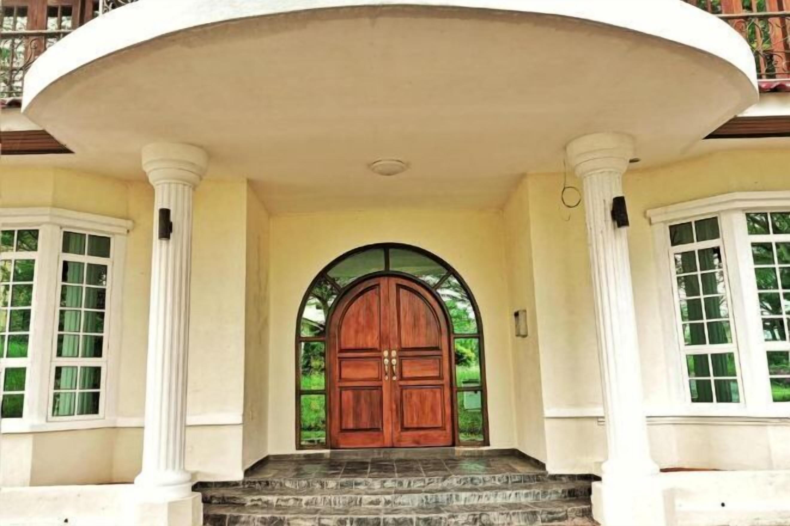 A grand entrance with a large wooden door, flanked by white columns and a semi-circular balcony.