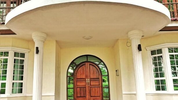 Una entrada imponente con una puerta de madera grande, flanqueada por columnas blancas y un balcón semicircular.