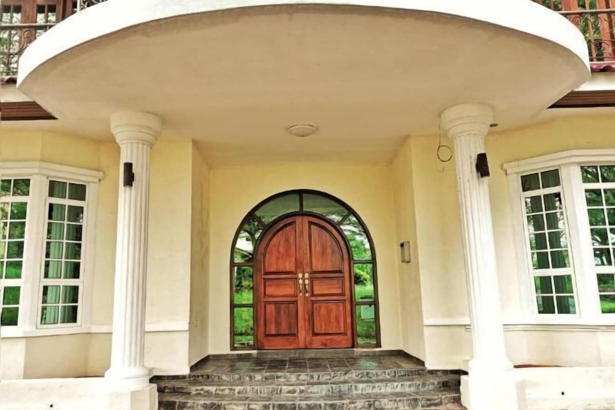 Una entrada imponente con una puerta de madera grande, flanqueada por columnas blancas y un balcón semicircular.