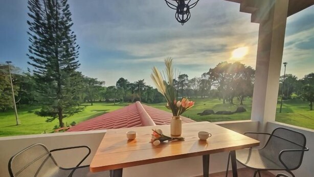 A table with chairs and a vase of flowers on a balcony with a view of a golf course. - Yussy Homestay at Afamosa Bungalow (Pegoh)