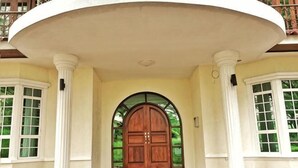 A grand entrance with a large wooden door, white columns, and a covered porch. - Yussy Homestay at Afamosa Bungalow (Pegoh)