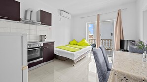 A compact hotel room with a kitchenette, a bed with bright green pillows, a balcony with curtains, and a dining area with a table and chairs. - Beautiful apartment in Vodice with WiFi (Vodice)
