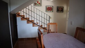 Uma escada com corrimão, uma cadeira de madeira e uma cama com cabeceira branca.